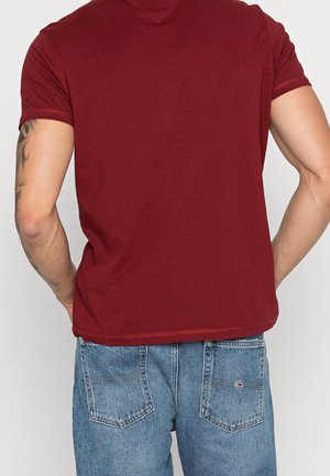 Vinrød t-shirt med korte ærmer og rund hals, kombineret med lyseblå cowboybukser med to baglommer og en lille logodetalje.