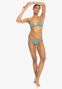 Zelené bikiny s trojuholníkovým vrchom a nízko strihanými nohavičkami. Tkanina je hladká s minimálnym prešívaním. Na vrchu sú nastaviteľné popruhy.