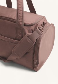 Brown fabric duffel bag with sturdy handles, a detachable strap, and a zipper closure. No visible patterns or accents.