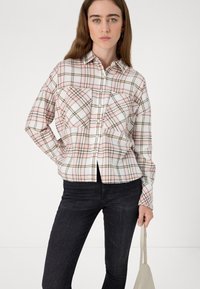 Camisa de padrão quadriculado em rosa pastel, branco e castanho. Apresenta dois bolsos no peito, fecho com botões e um corte descontraído. Combinada com jeans escuros.