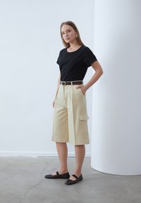 Svart bomull t-shirt med avslappnad passform; krämfärgade culottbyxor med sidfickor, strukturerad design; svarta platta skor med rund tå.