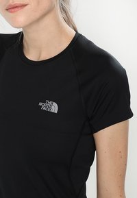 Svart atletisk t-shirt med korta ärmar, med en grå logotyp på vänster bröst och sömdetaljer för en figursydd look.