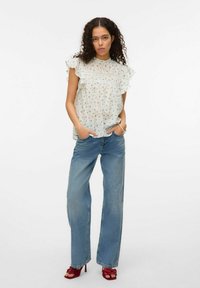 Blouse florale légère avec des manches à volants, associée à un jean bleu taille haute et ample, et des sandales à talons rouges.
