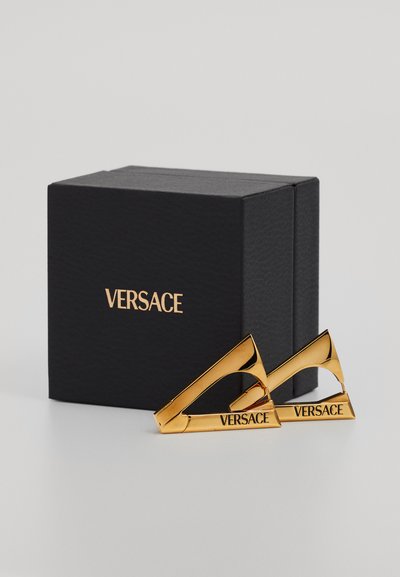 Auksinės spalvos metalinės segtukai kampuotame dizaine su išgraviruotu „VERSACE“. Juodas tekstūruotas dėžutė su iškilmingu prekės ženklu, uždaryta viršuje.