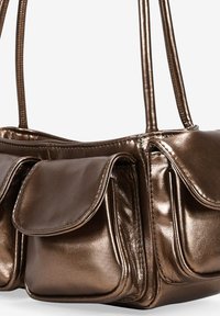 Bolso de mano de bronce metálico con dos asas cortas, que presenta tres bolsillos en forma de bolsa y una textura suave. Realzado con un acabado brillante.