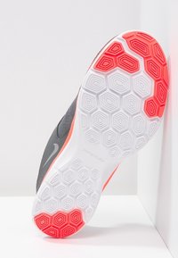 Nike Flex -kenkäpohja, jossa on kuusikulmainen kuvio valkoisena ja oransseja korostuksia. Yläosa on harmaata tekstiilimateriaalia, joka tarjoaa joustavuutta ja tukea.