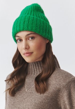 Beanie verde lavorato a maglia con un design a coste testurizzato. Indossato con un pullover a collo alto marrone chiaro con un'accenno a coste.