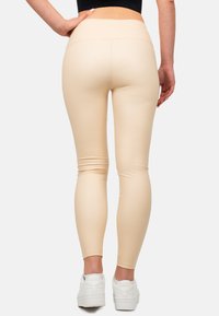 Leggings beige con una texture liscia e elastica e una vita alta, abbinati a scarpe da ginnastica bianche. Vista da dietro.