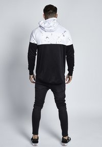 Svart hoodie med ett vitt marmor mönster på den övre delen, långa ärmar och en avslappnad passform. Kombinerad med slim fit svarta jeans och sneakers.