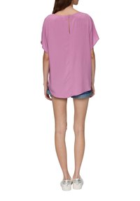 Losse, roze blouse met korte mouwen, een sleutelgatopening aan de achterkant en een zachte textuur. Gecombineerd met denim shorts en instappers.