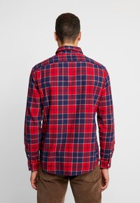 Camisa de cuadros roja y azul marino con mangas largas, cuello abotonado, corte clásico y dobladillo curvado. Tejido de algodón con una textura suave.