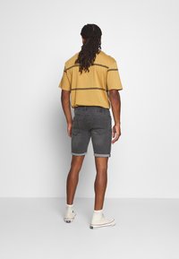 Grijze denim shorts met opgerolde zoom en een zwarte leren riem, gecombineerd met een mosterdgeel overhemd met korte mouwen en zwarte strepen.