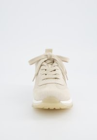 Béžové semišové tenisky s kulatou špičkou, texturovaným svrškem, plochými šňůrkami a bílou mezipodešví. Průhledná gumová podrážka viditelná na spodní části.