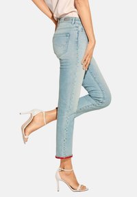 Hellblaue Denim-Jeans mit mittlerer Bundhöhe und rotem Pom-Pom-Besatz am Saum, kombiniert mit weißen, schnürbaren High Heels.