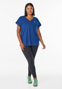 Mörkblå kortärmad T-shirt med V-ringning i mjukt material, matchad med svarta leggings och gröna sneakers, med en minimalistisk design.