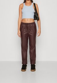 Haut court côtelé bleu clair associé à un pantalon en simili cuir bordeaux à cordon de serrage ; modèle portant des baskets noires et tenant un petit sac noir.