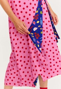 Růžové šaty s puntíky a modrou podšívkou se květinovým vzorem. Materiál je lehký a má splývavý design. Spodní lem je asymetrický.