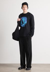 Tricou negru cu mâneci lungi și design grafic albastru, pantaloni negri cu potrivire lejeră, bentiță neagră și geantă de umăr neagră. Texturi fine pe întreaga compoziție.