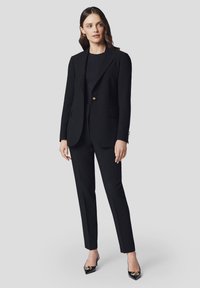 Czarny, dopasowany garnitur z uszytą marynarką i wąskimi spodniami. Posiada pojedynczy złoty guzik, proste nogawki oraz gładki, teksturowany materiał.