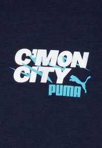 Námořnická modrá textilie s výrazným bílým a tyrkysovým nápisem "C'MON CITY" a "PUMA." Obsahuje malou siluetu loga Puma.