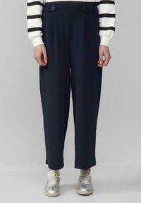 Marineblauwe hoge taillebroek met plooien en dubbele knoopaccenten. Het materiaal is zacht, met een relaxte pasvorm en een lengte tot de enkels, gecombineerd met lichte sneakers.