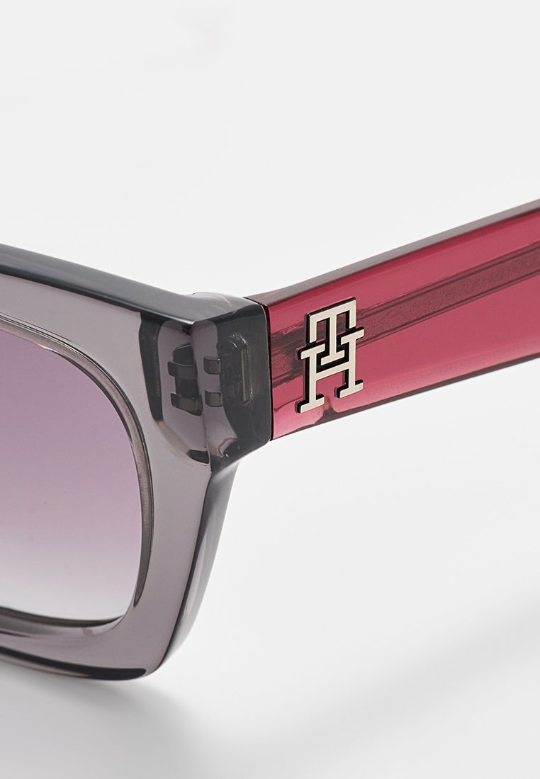 Sonnenbrille mit grau-schwarzen quadratischen Gläsern, einem glänzenden burgunderfarbenen Bügel mit silbernem Logo und einem eleganten Design. Strukturiertes Detail am Bügel.