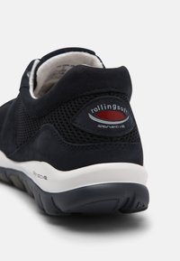 Donkerblauwe sneaker met bovenwerk van mesh en suède, gevoerde binnenkant, opvallend logo op de hiel en witte zool met een gestructureerd grippatroon.
