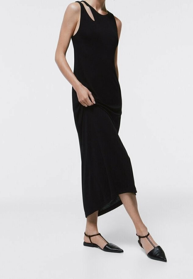 Robe noire sans manches avec découpe sur l'épaule, offrant une coupe décontractée et un ourlet asymétrique, associée à des ballerines noires pointues.