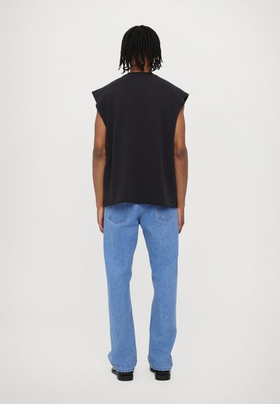 Melnas bezpiedurkņu blūze ar apaļu kakla izgriezumu; apvienota ar gaiši zilām taisnām biksēm. Audums izskatās gluds un ikdienišķs.