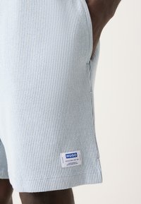Light blue ribbed shorts made of textured fabric with a side pocket and a branded white tag near the hem.