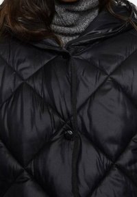 Sort dunjakke med diamantformet quiltet mønster, forside med knaplukning og fastsyet hætte. Fremstillet af skinnende, glat stof.