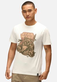 Bílý bavlněný tričko s vintage-stylovým hnědým grafikou Ewoka s textem "STAR WARS" nad ním, doplněné zbraněmi a akcenty postavy.