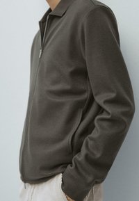 Giacca grigia con zip, collo con rever, maniche lunghe, tessuto morbido e design minimalista, con tasche laterali e vestibilità comoda.