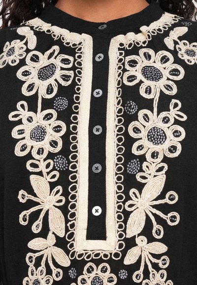 Fekete anyagú felső, bonyolult krémszínű virágmintával hímezve, fekete gombos záródással az elején, lekerekített gallér kialakítással.