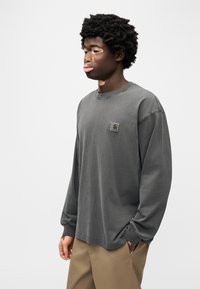 Γκρι μακρυμάνικη μπλούζα με στρογγυλή λαιμόκοψη και άνετη εφαρμογή. Διαθέτει μικρό λογότυπο στο στήθος, σε συνδυασμό με μπεζ παντελόνια.