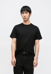 Čierne tričko s krátkym rukávom z bavlneného materiálu, s okrúhlym výstrihom, v kombinácii s čiernymi nohavicami a čiernym opaskom. Jednoduchý strih a jednofarebné prevedenie.