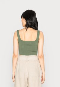 Top cropped canelado verde-oliva com decote quadrado, combinado com calças bege claras de cintura alta com bolsos laterais e um cós justo.