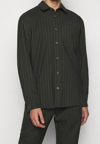 Mörkgrön skjorta med knappar och subtila vertikala ränder, långa ärmar och en bröstficka. Tillverkad av ett mjukt material med en strukturerad passform.