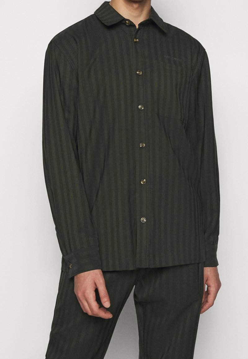 Mörkgrön skjorta med knappar och subtila vertikala ränder, långa ärmar och en bröstficka. Tillverkad av ett mjukt material med en strukturerad passform.