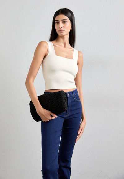 White cropped top with square neckline, paired with dark blue jeans. Model holds a textured black clutch bag. Neutral background.