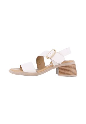 Sandalias de tacón blancas con dos tiras anchas y una hebilla dorada. Los tacones son de forma rectangular con una textura similar a la de la madera y de color marrón claro.