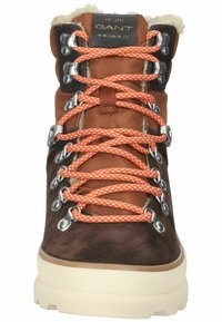 Brown suede hiking boot with orange laces, silver eyelets, and beige sole. Features a soft lining and branded tongue for added detail.