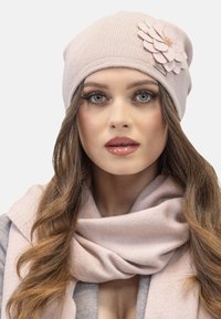 Căciulă ribbed de culoare roz deschis, cu un accent de floare din fetru, asociată cu o eșarfă roz asortată. Textură netedă, design ajustat.