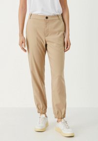 Beiga joggerbyxor i mjukt tyg med elastiska muddar, en framknäppning och sidofickor, tillsammans med vita sneakers.