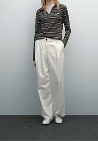 Haut à manches longues, sans col, à rayures grises avec des accents marron ; pantalon large blanc ; chaussures blanches ; texture lisse, coupe décontractée.