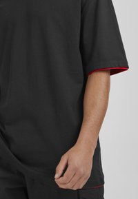 Camiseta negra de manga corta, con acentos rojos en los puños. Hecha de algodón con una textura suave y un corte relajado.