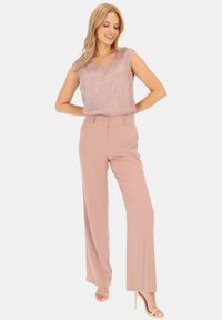 Jasnoróżowy top bez rękawów o teksturowanym wykończeniu, zestawiony z różowymi spodniami o szerokich nogawkach i wysokim stanem. Całość dopełniają neutralne szpilki.