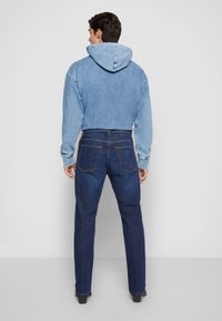 Denim hoodie in light blue, featuring a drawstring hood, and dark blue jeans with a straight leg and back pockets, displayed from the back.