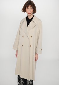 Beige double-breasted coat with large lapels, gold buttons, and wide sleeves, featuring a loose fit and smooth fabric texture.