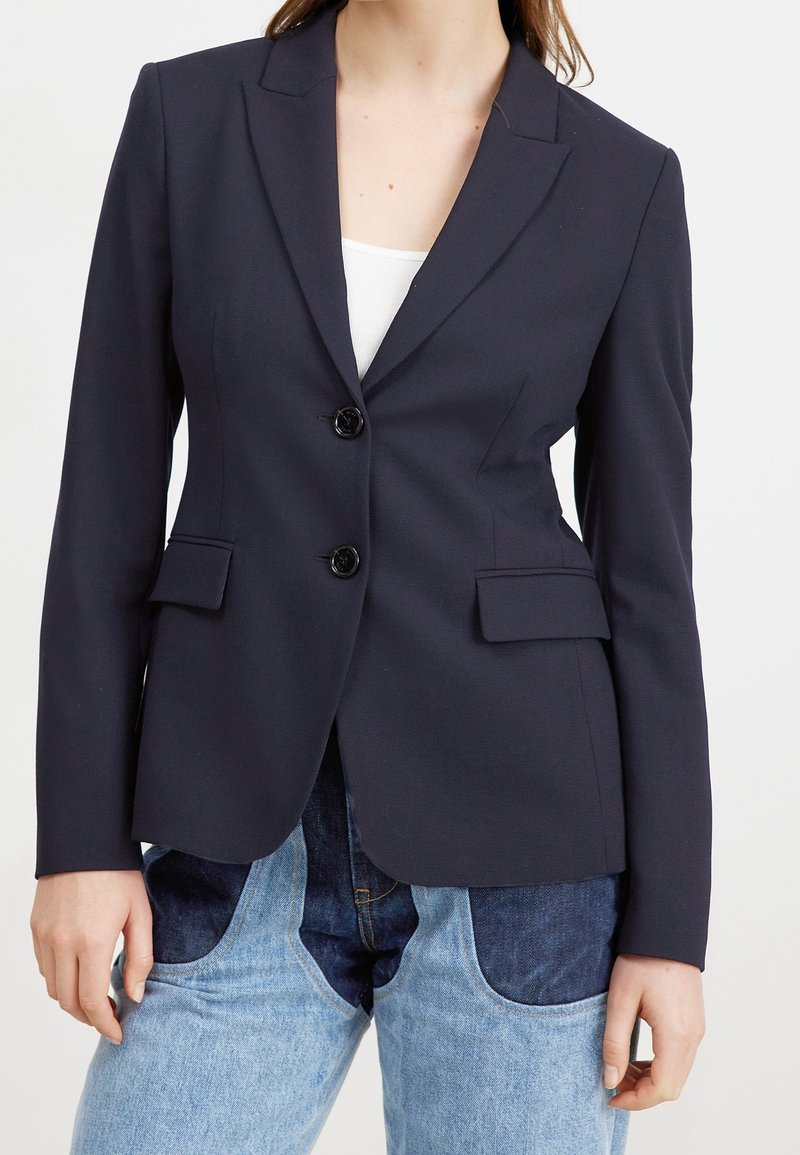 Granatowa marynarka wykonana z teksturowanej tkaniny, z dwoma kieszeniami z przodu, dwoma guzikami i klapą z wyci�ęciem. Noszona na białej bluzce i dżinsach.